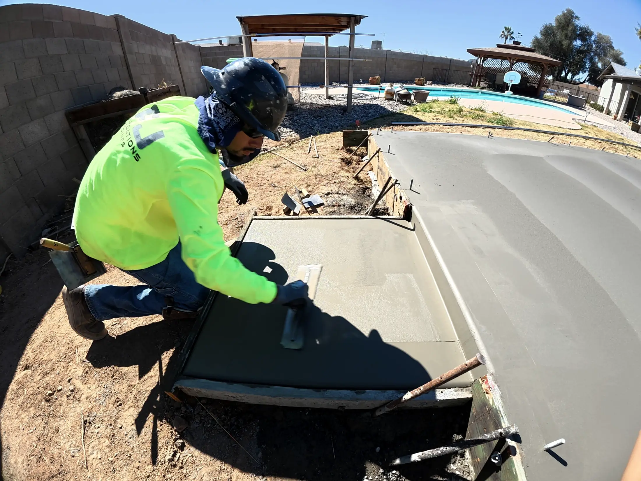 A crew member edging a new slab beside a backyard pool